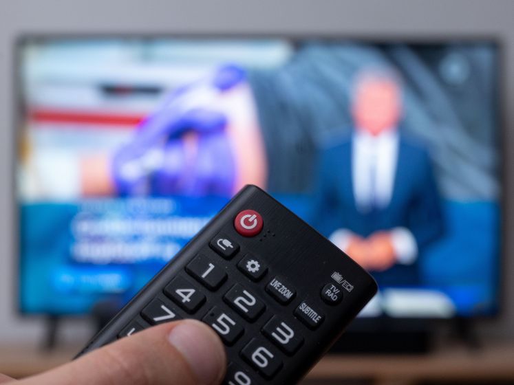 Ein Mann hält eine Fernbedienung vor einen Fernseher, auf dem die Tagesschau läuft.