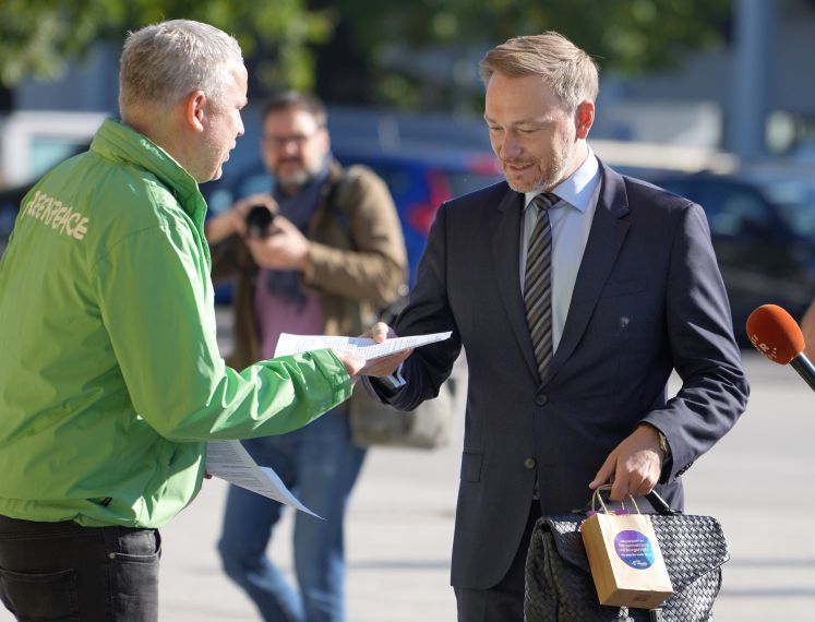 Christian Lindner nimmt von einem Greenpeace-Aktivisten ein Flugblatt entgegen.
