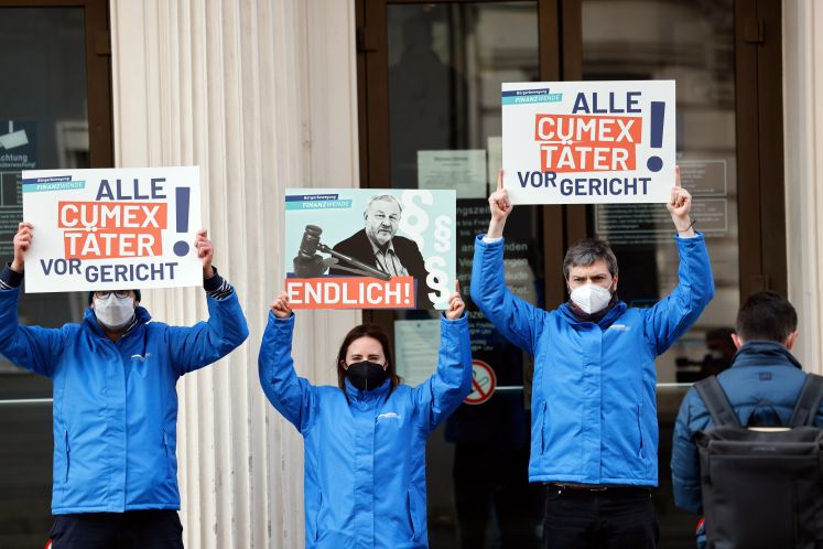 Aktivisten der „Bürgerbewegung Finanzwende jetzt“ halten vor dem Landgericht Plakate mit der Aufschrift „Alle Cumex Täter vor Gericht“