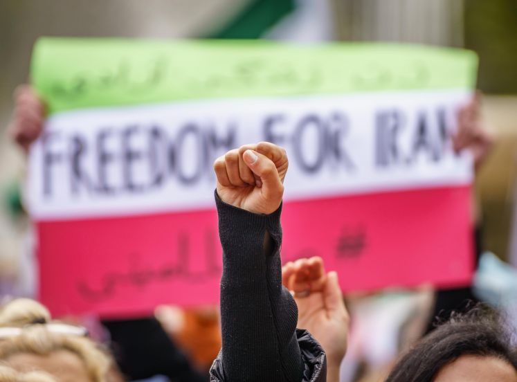 Eine Faust reckt sich vor einem Plakat mit der Aufschrift "Freedom for Iran"