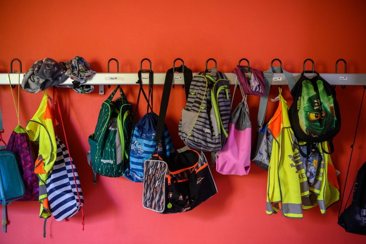 Bunte Kinderjacken und -rucksäcke hängen in der Schule an der Garderobe