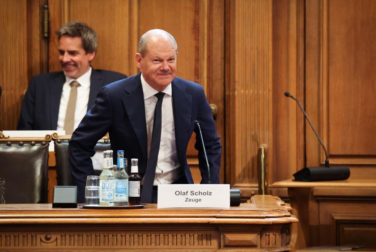 Bundeskanzler Olaf Scholz (SPD) sitzt auf seinem Platz auf der Senatsbank mit einem Plastikschild mit dem Text „Olaf Scholz Zeuge“ vor Beginn einer Sitzung des Parlamentarischen Untersuchungsausschusses „Cum-Ex“ im Plenarsaal der Hamburgischen Bürgerschaft im Rathaus.