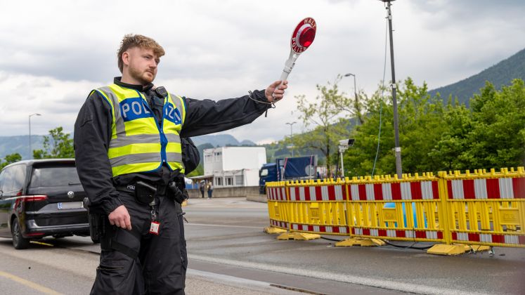 Polizist mit Warnweste hält eine Kelle und stoppt Autos an einer Straßensperre