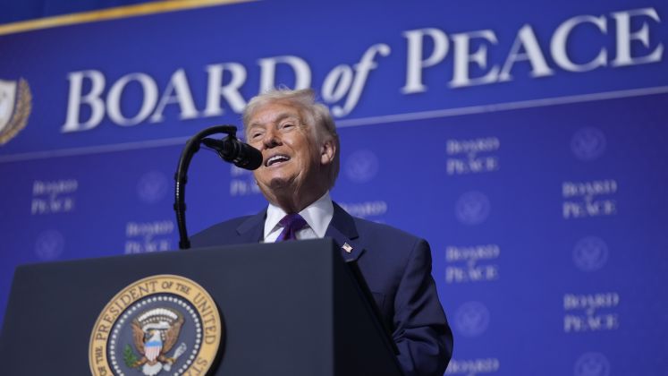 Foto: Donald Trump spricht lächelnd an einem Rednerpult vor blauem Hintergrund.