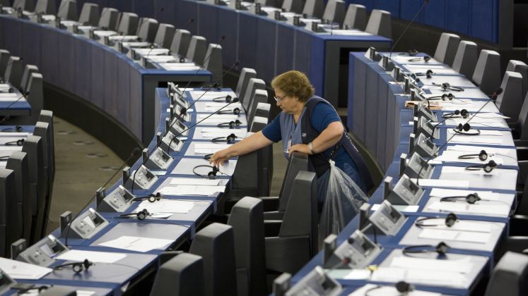 Frau in blauer Kleidung reinigt leere Sitze in einem großen Saal, vermutlich Parlament