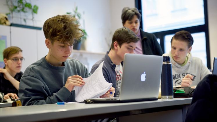 Jugendliche arbeiten im Klassenzimmer, Laptops und Unterlagen auf dem Tisch. Foto.