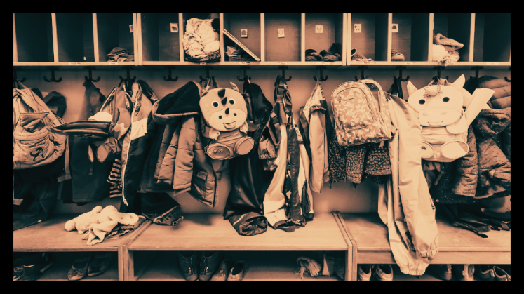 Foto: Garderobe mit vielen Kinderjacken, Rucksäcken und Mützen, keine Personen erkennbar.