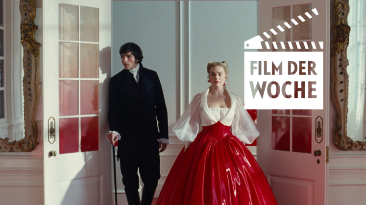 Mann im schwarzen Anzug und Frau im roten Kleid betreten prunkvollen Raum