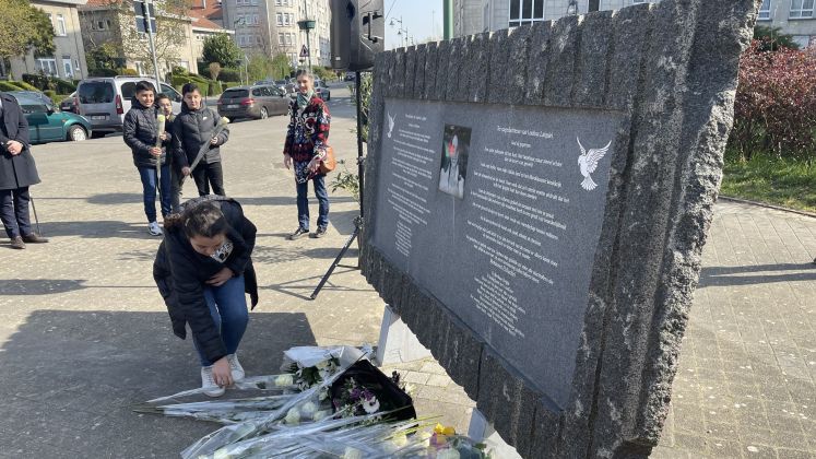 Frau legt Blumen an einer Gedenktafel nieder, mehrere Menschen stehen im Hintergrund, Foto.