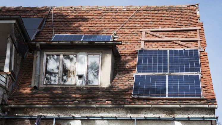 Foto eines Hausdachs mit mehreren Solarpanelen auf roten Ziegeln und Fenstern.
