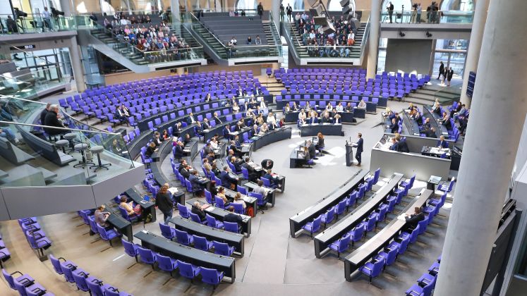 Foto; Plenarsaal des Bundestags mit vielen Abgeordneten auf blauen Sitzen, Redner am Pult.