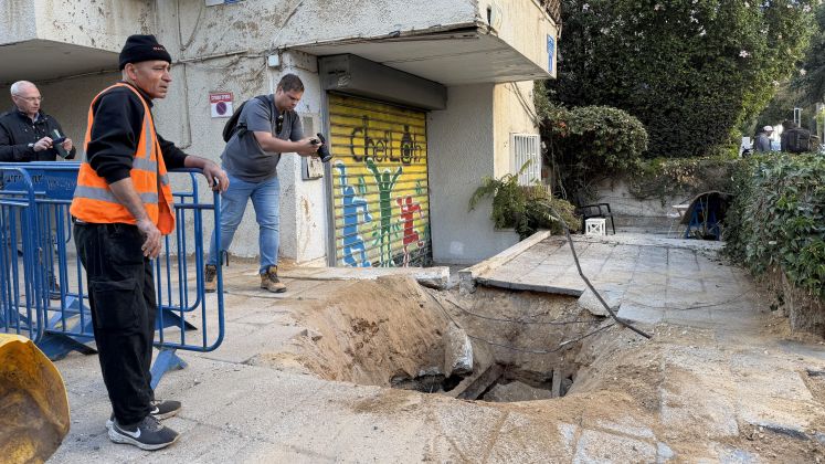Drei Männer bei einem Einschlagskrater auf Gehweg vor einem Gebäude, Foto
