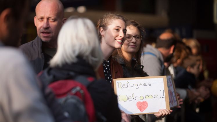 Mehrere Menschen stehen zusammen, eine Frau hält ein Schild, freundliche Atmosphäre, Foto.
