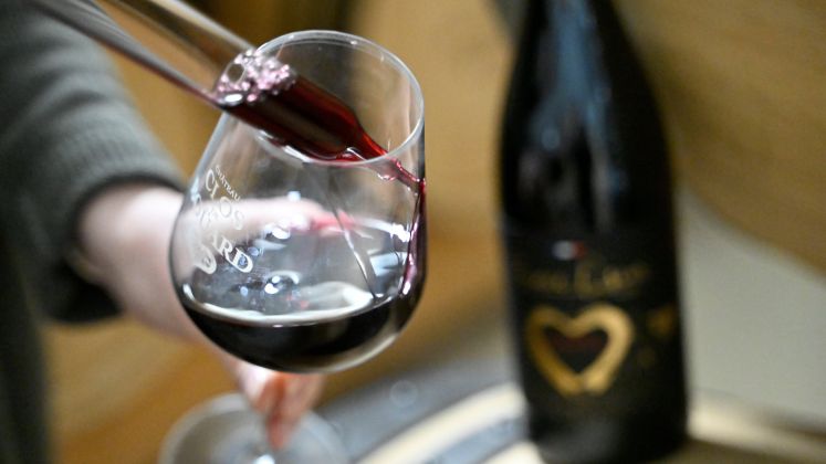 Wein wird in ein Glas gegossen, unscharfe schwarze Flasche mit goldenem Herz im Hintergrund, Foto.