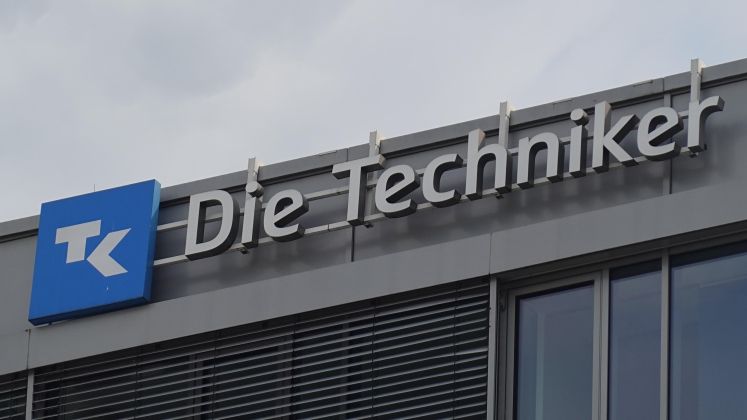Logo und Schriftzug "Die Techniker" auf einer modernen Gebäudefassade, Foto.