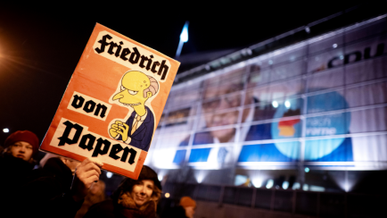 Auf einem Schild der Demonstranten wird Friedrich Merz in Anlehnung an Franz von Papen karikiert, den Reichskanzler, der Hitlers Machtübernahme begünstigte