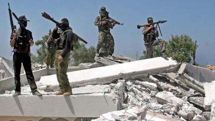 Vier bewaffnete, maskierte Männer stehen auf Trümmern; sonnige Außenaufnahme, Foto.