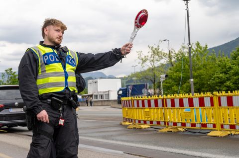 Polizist mit Warnweste hält eine Kelle und stoppt Autos an einer Straßensperre