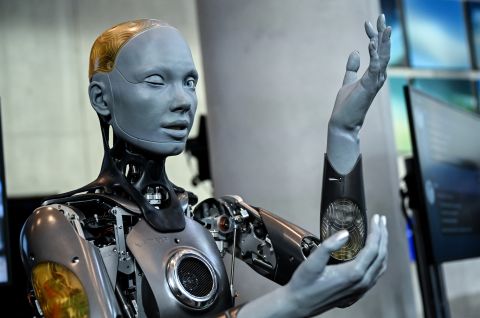 Foto eines humanoiden Roboters mit grauer Haut und sichtbaren mechanischen Teilen, hebt den Arm.