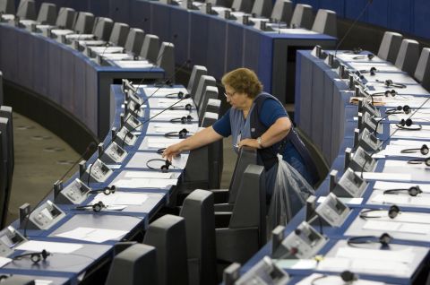 Frau in blauer Kleidung reinigt leere Sitze in einem großen Saal, vermutlich Parlament