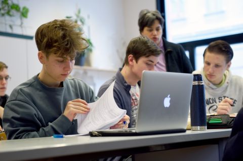 Jugendliche arbeiten im Klassenzimmer, Laptops und Unterlagen auf dem Tisch. Foto.
