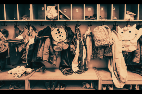 Foto: Garderobe mit vielen Kinderjacken, Rucksäcken und Mützen, keine Personen erkennbar.