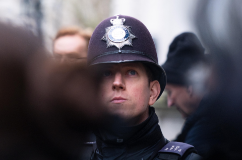 Britischer Polizist mit Helm in Uniform; unsicherer Vorschlag: weitere Personen im Hintergrund. Foto.