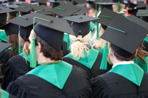 Foto: Viele Absolventen in schwarzen Roben und Hüten bei einer Abschlussfeier, Rückenansicht.