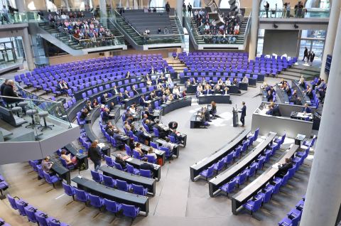 Foto; Plenarsaal des Bundestags mit vielen Abgeordneten auf blauen Sitzen, Redner am Pult.