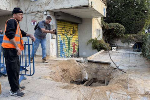 Drei Männer bei einem Einschlagskrater auf Gehweg vor einem Gebäude, Foto