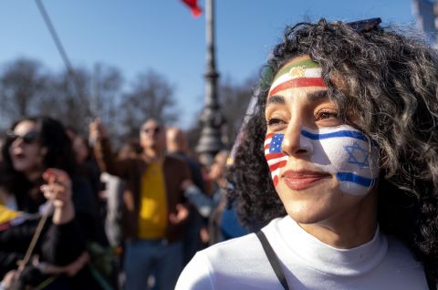 Frau mit bemaltem Gesicht in israelischen Farben, Menschenmenge im Hintergrund, Foto.