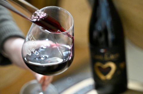 Wein wird in ein Glas gegossen, unscharfe schwarze Flasche mit goldenem Herz im Hintergrund, Foto.