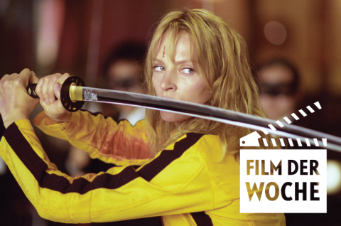 Foto: Uma Thurman im gelben Kampfanzug hält ein Katana, angespannt, unscharfer Hintergrund.