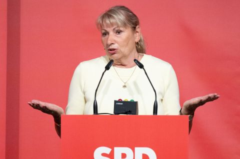 Frau am SPD-Rednerpult gestikuliert im cremefarbenen Blazer vor rotem Hintergrund, Foto.