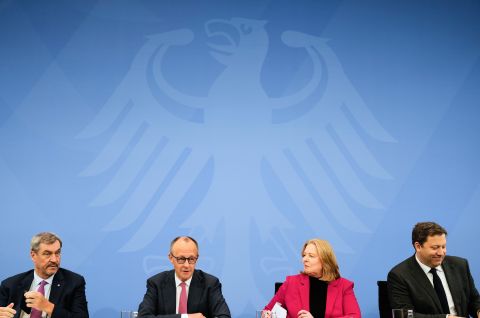 Vier Personen sitzen an einem Tisch vor einer blauen Wand mit Bundesadler, Foto.