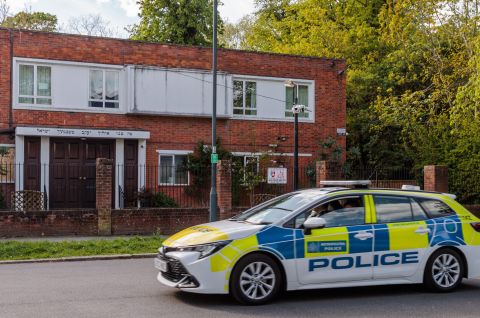 Polizeiauto steht vor einer Synagoge an einer Straße, grüne Bäume im Hintergrund; Foto.