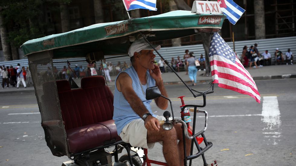 Ein Mann auf seiner Fahrradrikscha mit kubanischen und US-amerikanischen Nationalflaggen