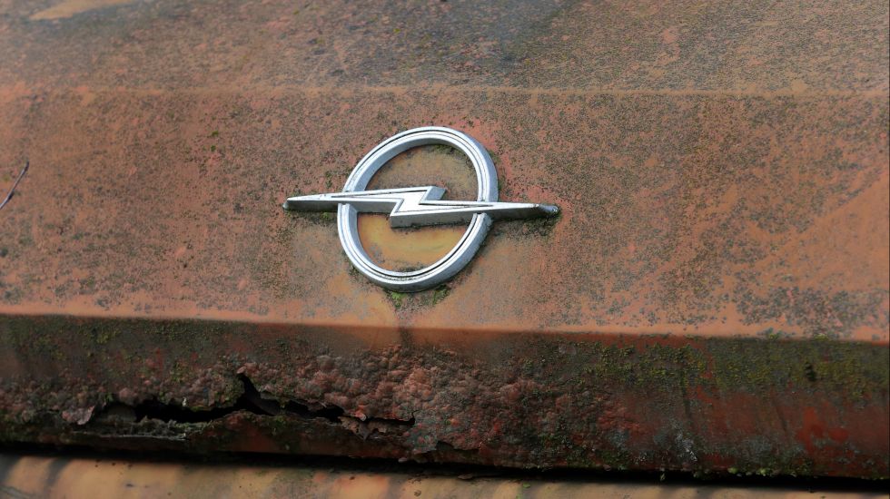 Eine rostige Motorhaube eines Opel-Fahrzeugs mit dem Blitzemblem 
