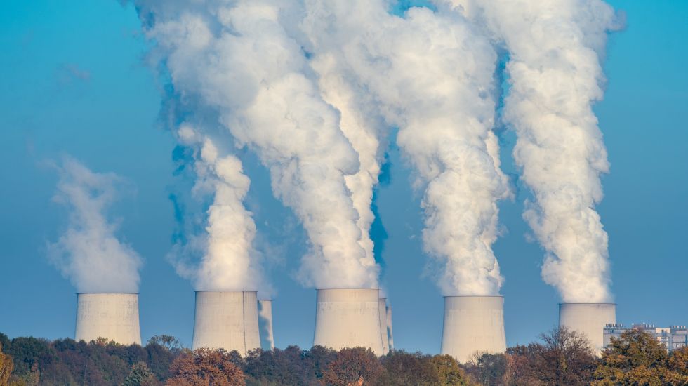 Neben einem malerischen Dorf im Wald entlässt ein riesiges Braunkohlekraftwerke Wasserdampf in die Luft