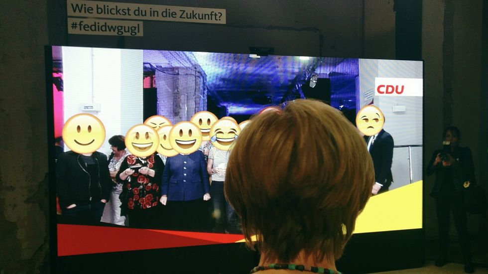 Merkel steht vor der Emoji-Wand im fedidwgugl-Haus in Berlin Mitte.