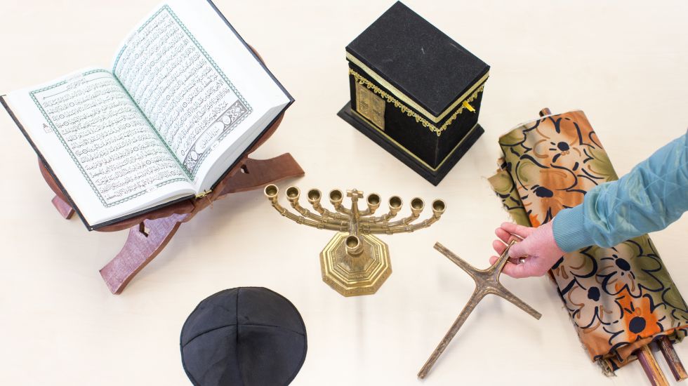 Symbole der drei Religionen Islam, Judentum und Christentum (Koran mit Koranständer (l-r), Kippa Kopfbedeckung, Chanukkaleuchter, Kaaba "Würfel", Kreuz und Torarolle) liegen am 23.11.2017 auf einem Tisch der Drei-Religionen-Schule in Osnabrück (Niedersachsen).