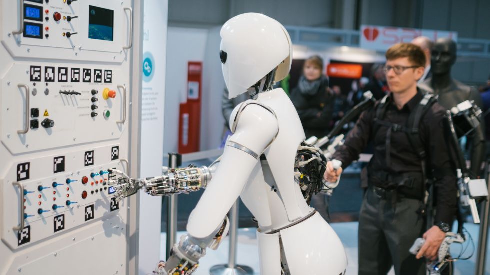 Ein Mitarbeiter des Robotic Innovation Centers steuert am 20.03.2017 bei der CeBIT Messe in Hannover (Niedersachsen) am Stand des deutschen Forschungszentrums für Künstliche Intelligenz (DFKI) mit Hilfe eines Exoskeletts den Roboter AILA.