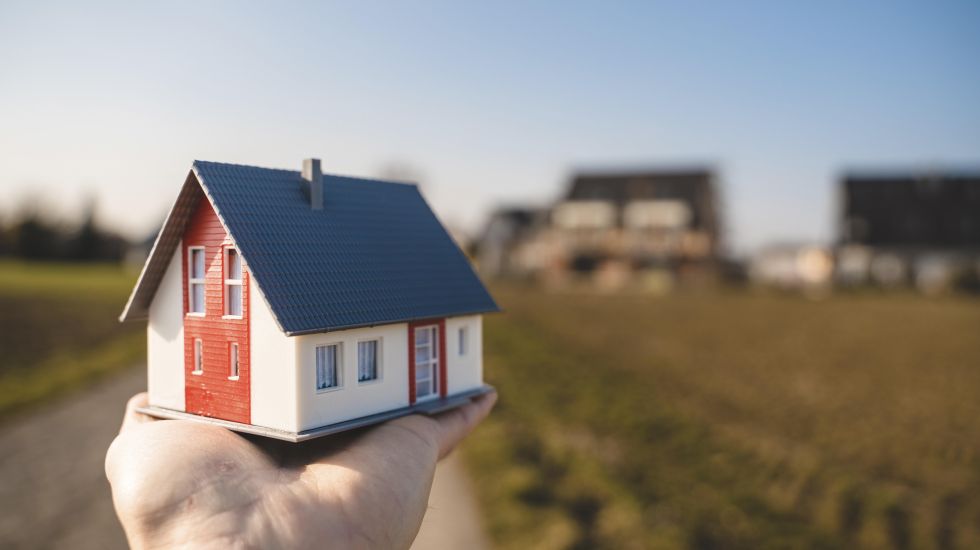 Eine Person hält ein Miniatur-Modell eines Eigenheims in die Kamera