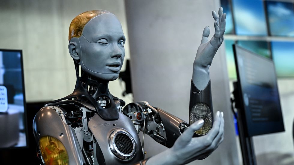 Foto eines humanoiden Roboters mit grauer Haut und sichtbaren mechanischen Teilen, hebt den Arm.