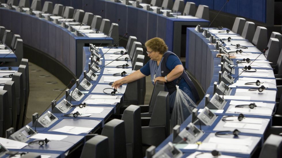 Frau in blauer Kleidung reinigt leere Sitze in einem großen Saal, vermutlich Parlament