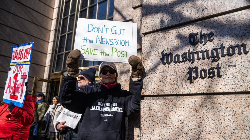 Foto: Mehrere Personen protestieren vor dem Washington Post Gebäude mit Schildern, winterlich gekleidet.
